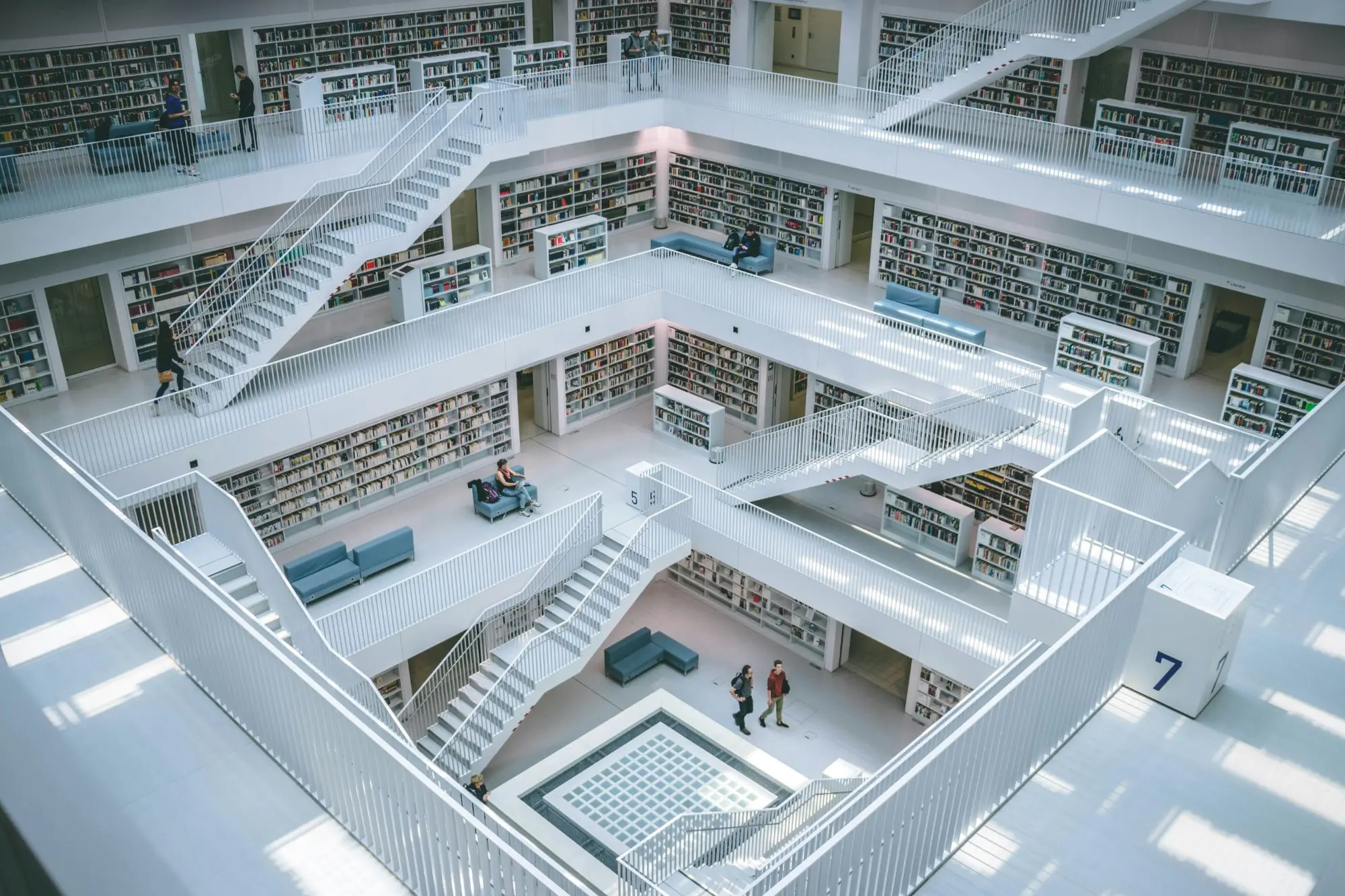 A white, multi-storey library seen from above, with stairs, walkways and shelves of books